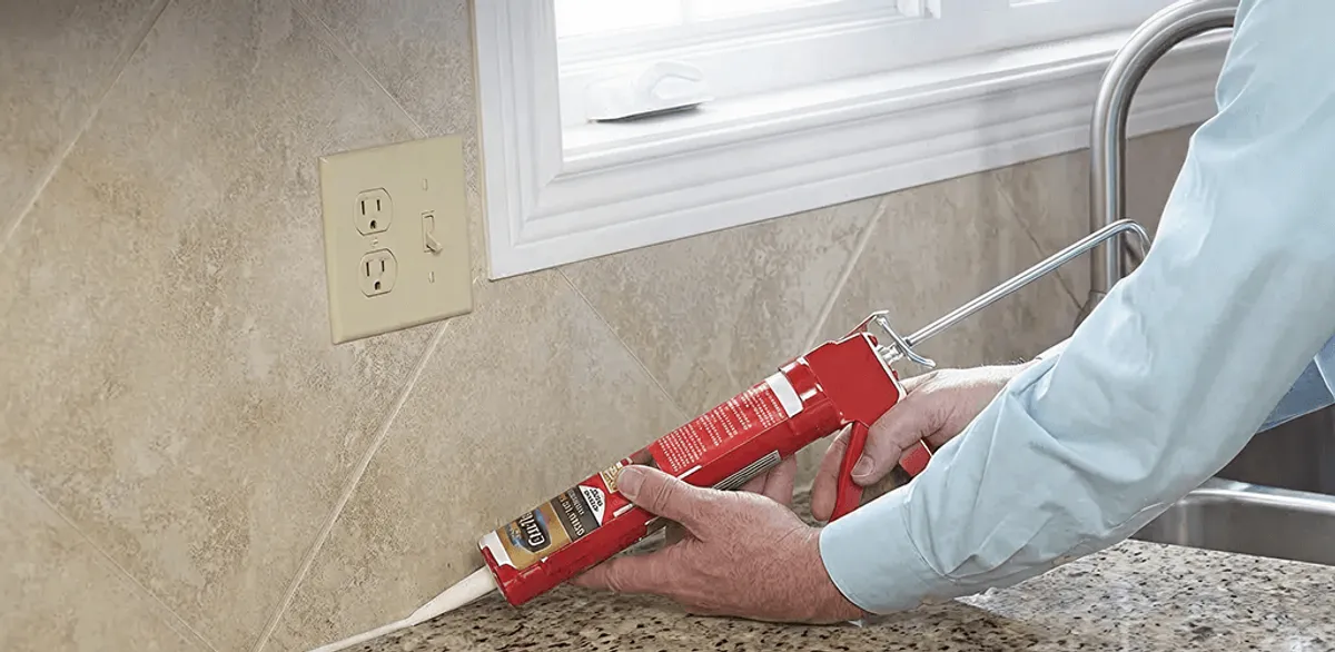 Handyman applying caulk along a kitchen backsplash and countertop seam in Birmingham, AL